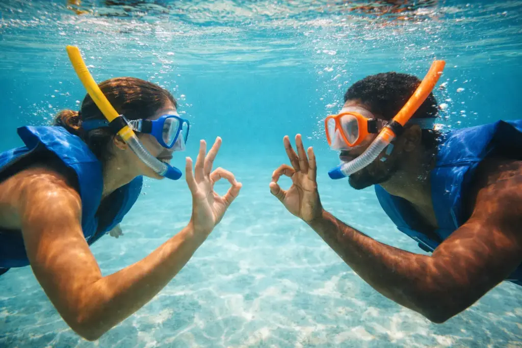 Two snorkelers signaling each other underwater in clear ocean water demonstrating the buddy system.